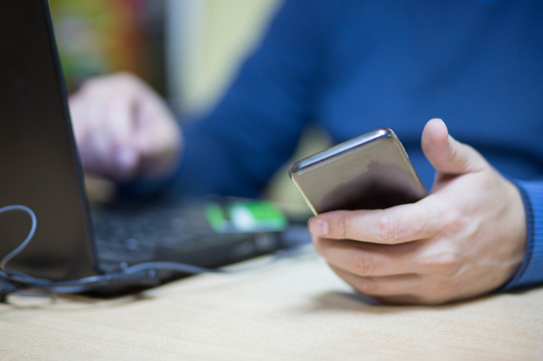 Man with a phone in his hand, sitting at a laptop