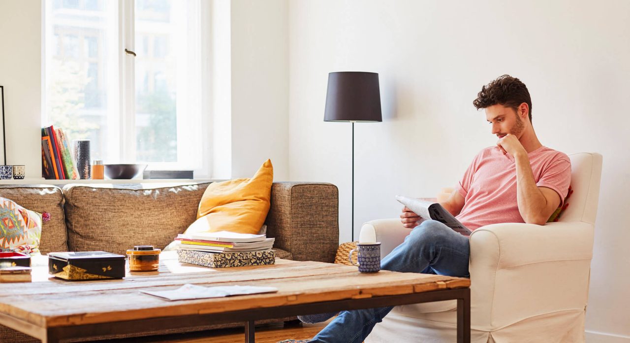 man reading newspaper in living room armchair