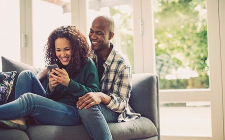 Young couple on sofa at home laughing at phone